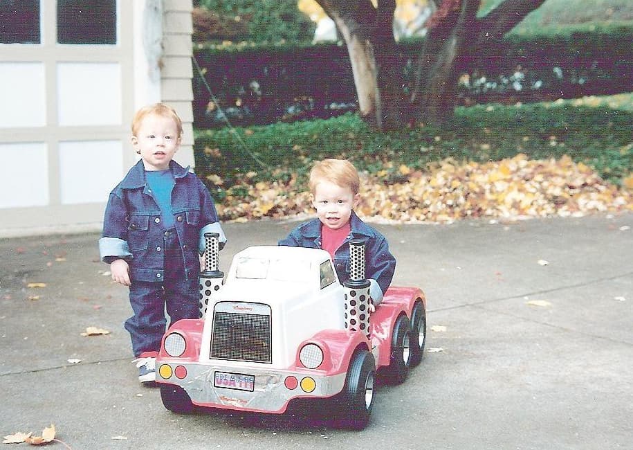 Matt Convente and Mike Convente as toddlers in their driveway driving a Power Wheels 18 wheeler truck cab.